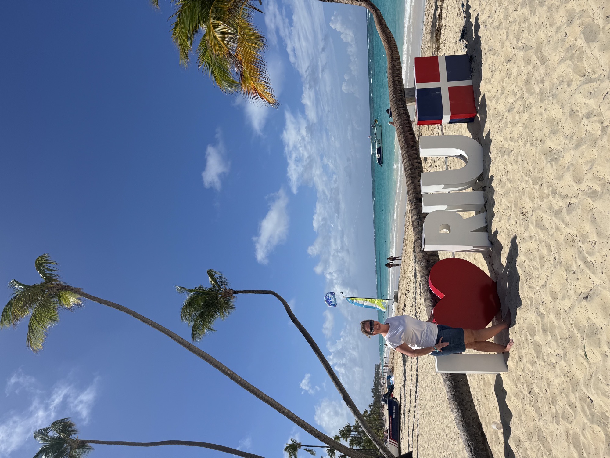 Liz beside an I love RIU sign on a beach in the Dominican Republic