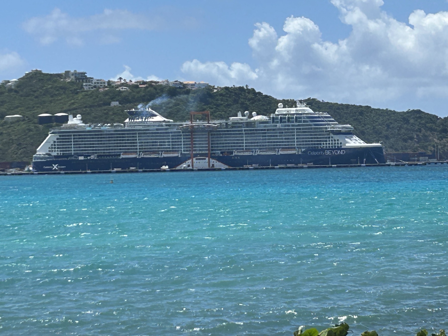 The Celebrity Beyond docked against a green hillside and turquoise water