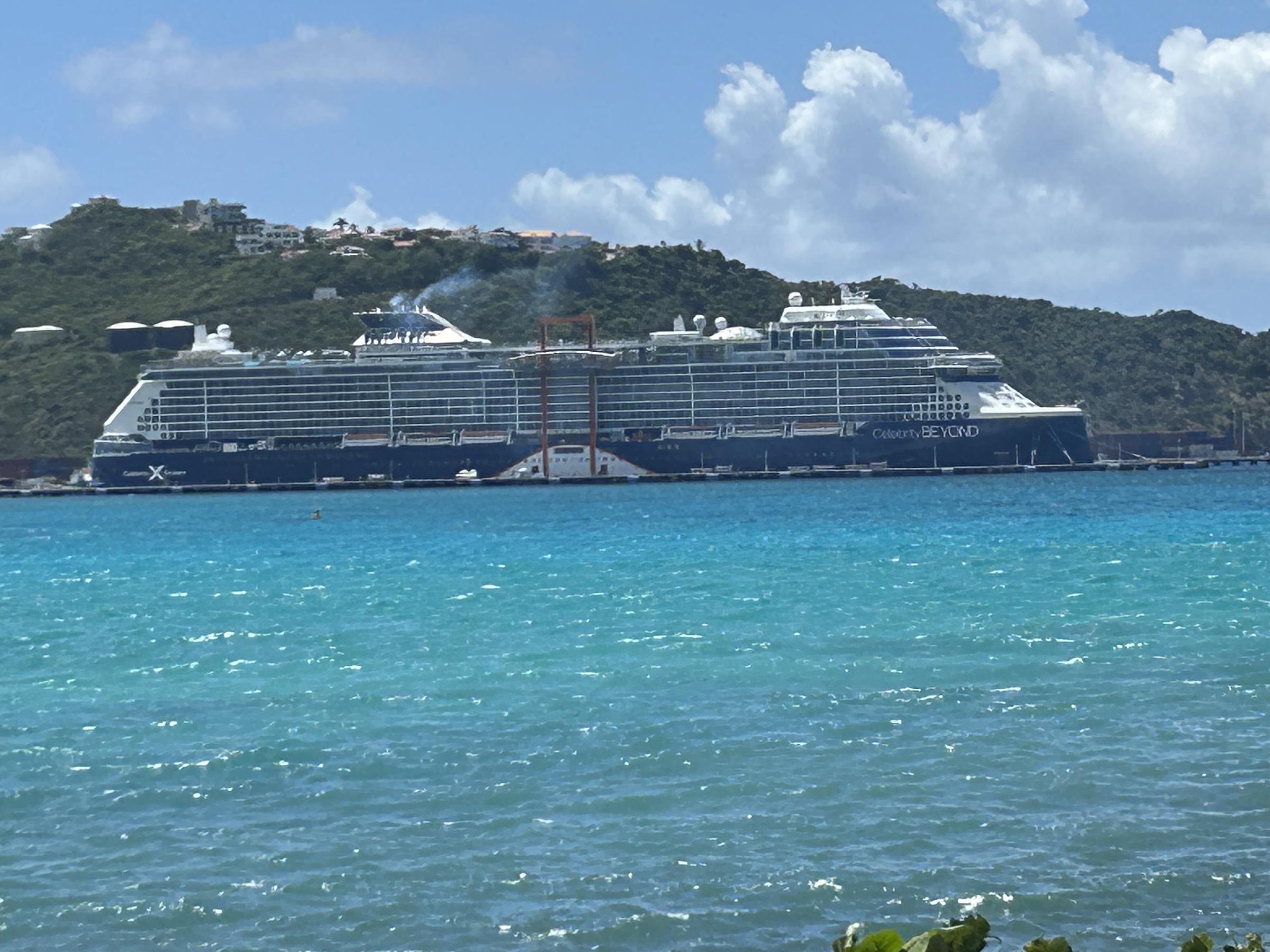 The Celebrity Beyond docked against a green hillside and turquoise Caribbean water
